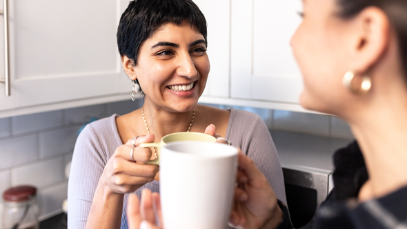 close up of happy woman talking to friend and drinking coffee