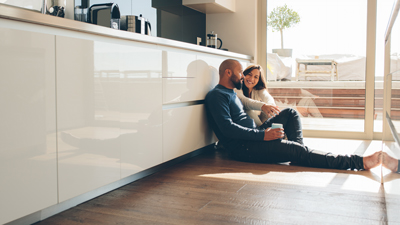 young happy couple sitting on floor of kitchen with cup of tea