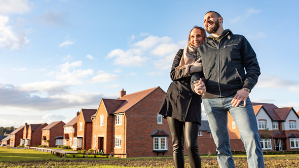 couple in coats smiling with new build estate in background