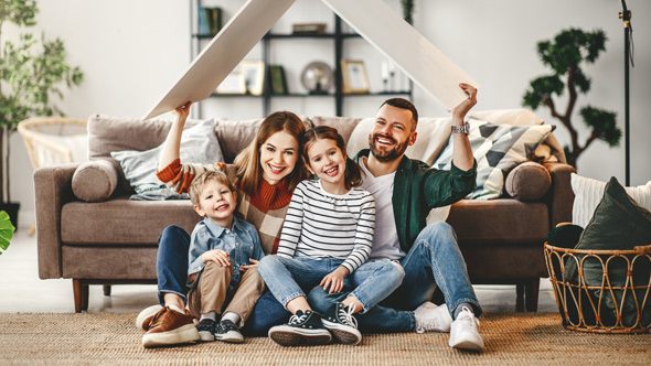 young happy family sat on floor of living room with wooden roof over head